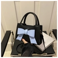 Detail of elegant black tote bag featuring a prominent light blue bow and metal hardware - Black with Blue