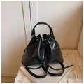 Detail of black glossy patent leather bucket bag with drawstring and top handle on a white marble - Black