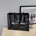 Black mesh tote bag with THE BEACH BAG print on a minimalist wooden background - Black With White Lettering
