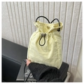 Minimalist pale yellow drawstring bucket bag with black strap on a leather sofa - Yellow