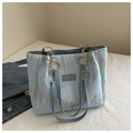 Close-up of light blue tote bag featuring colorful embroidery and logo metal plaque - Blue