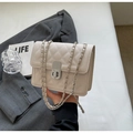 Dettaglio borsa trapuntata beige con catena e chiusura a rotazione su sfondo di classe - Bianco Sporco