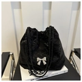 Detalle del bolso tipo saco negro con cordón y un lazo plateado en tejido texturizado - Negro