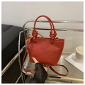 Detail of red lychee grain leather bucket bag featuring unique knotted handle design - Red Without Charm