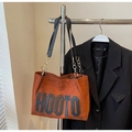 Caramel brown suede tote bag with HOOTO lettering and gold chain strap hanging on a rack - Coffee