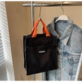 Close-up of black canvas bag with orange handles, front pocket and zipper closure detail - Black