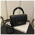 Bolso acolchado negro con asa fruncida y detalles dorados sobre un libro - Negro