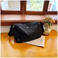 Minimalist black nylon crossbody bag with wide strap and fashion tag on wooden table - Black
