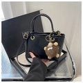 Close-up of black patent leather bucket bag with metal handle and plush monster charm - Black With Pendant