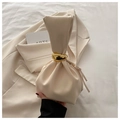 Bolso cubo plisado beige con asa de anillo dorado sobre un fondo de blazer suave - Blanco