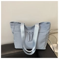 Light blue nylon tote bag with wide shoulder strap and woven zipper pull on black sofa - Blue