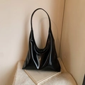Glossy black hobo bag with minimalist design on a book in an art gallery setting - Black
