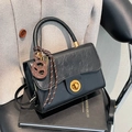 Black leather small square bag with golden buckle and pretzel charm in a lifestyle setting - Black With Pendant