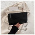 Black woven leather crossbody bag with silver chain strap on a white blazer background - Black