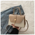 Modische zweifarbige Handtasche in Beige und Creme mit goldener Schnalle auf Bett - Khaki