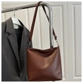 Detalle de bolso tote de cuero marrón con correa ajustable y elegantes pliegues - café