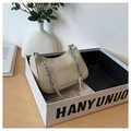 Detail of beige woven hobo bag with silver chain strap on a minimalist tabletop setting - Off White