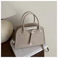 Close-up of beige PU leather handbag with silver hardware and top handle on books - Khaki