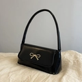 Glossy black baguette bag with gold bow buckle in a minimalist side-view presentation - Black