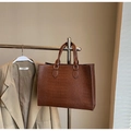 Détail de la texture d'un sac cabas marron à motif crocodile suspendu à un portant - café