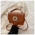 Brown leather handbag with diamond-encrusted buckle and top handle shown in lifestyle context - Brown