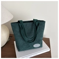 Primer plano del bolso tote de pana verde oscuro con textura y etiqueta de marca - Verde