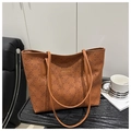 Close-up of brown leather tote bag with embossed floral texture on a dark wooden table - Brown