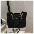 Détail du sac cabas noir avec chaîne dorée et logo de marque sur fond de livre - Noir