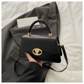 Detailed close-up of a luxury black leather handbag with a gold metal logo clasp - Black