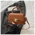 Détail du sac en cuir caramel avec fermoir doré en V sur une veste de costume grise - Marron