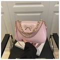 Close-up of pink leather handbag featuring a golden bow buckle and dual chain accents - Pink