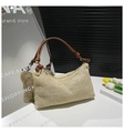 Detail of straw woven tote showing crescent shape, brown leather strap and knot accent - Brown