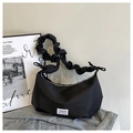 Detalle del bolso de media luna negro con asa plisada y etiqueta de moda sobre tela vaquera - Negro