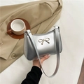 Silver metallic hobo bag with gold bow buckle held against a khaki trench coat - Silver