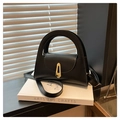 Detail of a black structured handbag with gold geometric clasp and long strap on books - Black