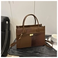 Detail van een bruine tote bag met krokodillenprint en gouden metalen draaisluiting - koffiekleur