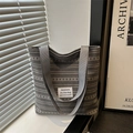 Chic grey striped fabric tote bag with shoulder straps and fashion label in soft daylight - Gray