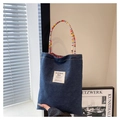 Dark blue denim tote bag with colorful braided handles and a woven logo patch - Small