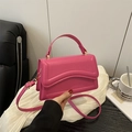 Rose red square crossbody bag with wavy stitching and top handle shown in lifestyle setting - Pink