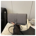 Detalle de bolso bandolera gris texturizado con hebilla cuadrada en un ambiente informal - Negro