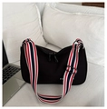 Black crescent nylon crossbody bag with striped wide strap on white bedding backdrop - Black