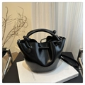Close-up of black glossy bucket bag with knotted ring handles on an art book background - Black