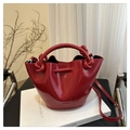 Detail of red leather bucket bag with knotted handle on white books in aesthetic setting - Red