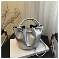 Detail of silver bucket bag featuring a knotted handle and sleek metallic texture on a book - Silver