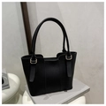 Black lychee leather bucket bag with gold hardware and curved handles on books - Black