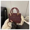Detail van bordeauxrode handtas met slangenstructuur, gevlochten handvatten en goud - Rood