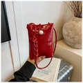 Close-up of red patent leather crossbody bag with a large pearl buckle and braided strap - Red