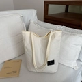 Bolso tote de lona plisada beige con etiqueta de logo negro en sofá blanco - Blanco