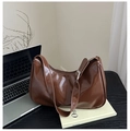 Detail der braunen glänzenden Mondsichel-Achseltasche mit Silberschnalle auf dem Tisch - Braun