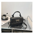 Close-up of black crossbody bag with wavy flap edge, gold bow, and knotted handle - Black